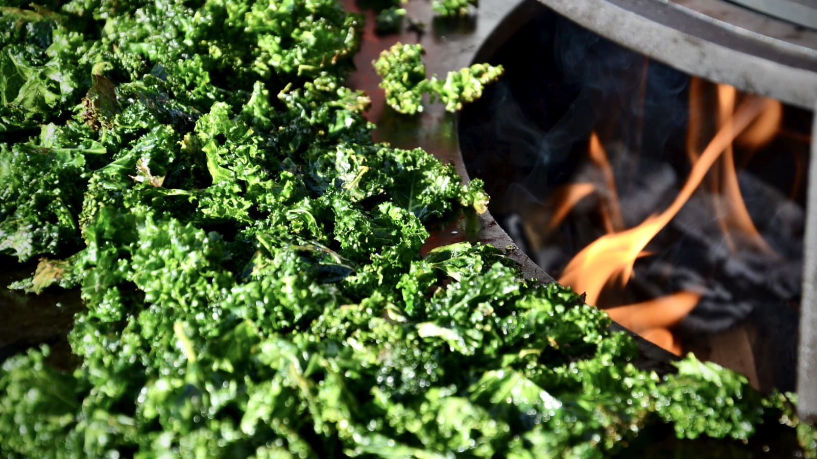 Crispy kale chips roasting on the OFYR grill plate over the autumn fire – a seasonal snack and perfect apéro treat with a smoky touch.