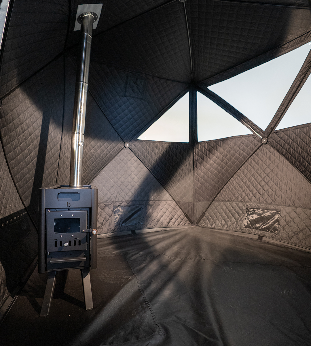 Wood-burning stove in a Bast Sauna tent with geometric wall design and removeable floor.
