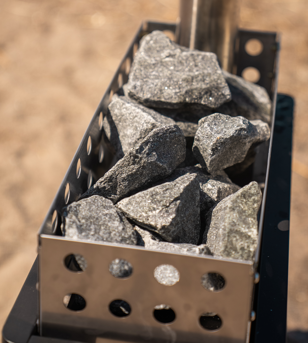 Metal sauna stone basket filled with rocks on a blurred natural background.