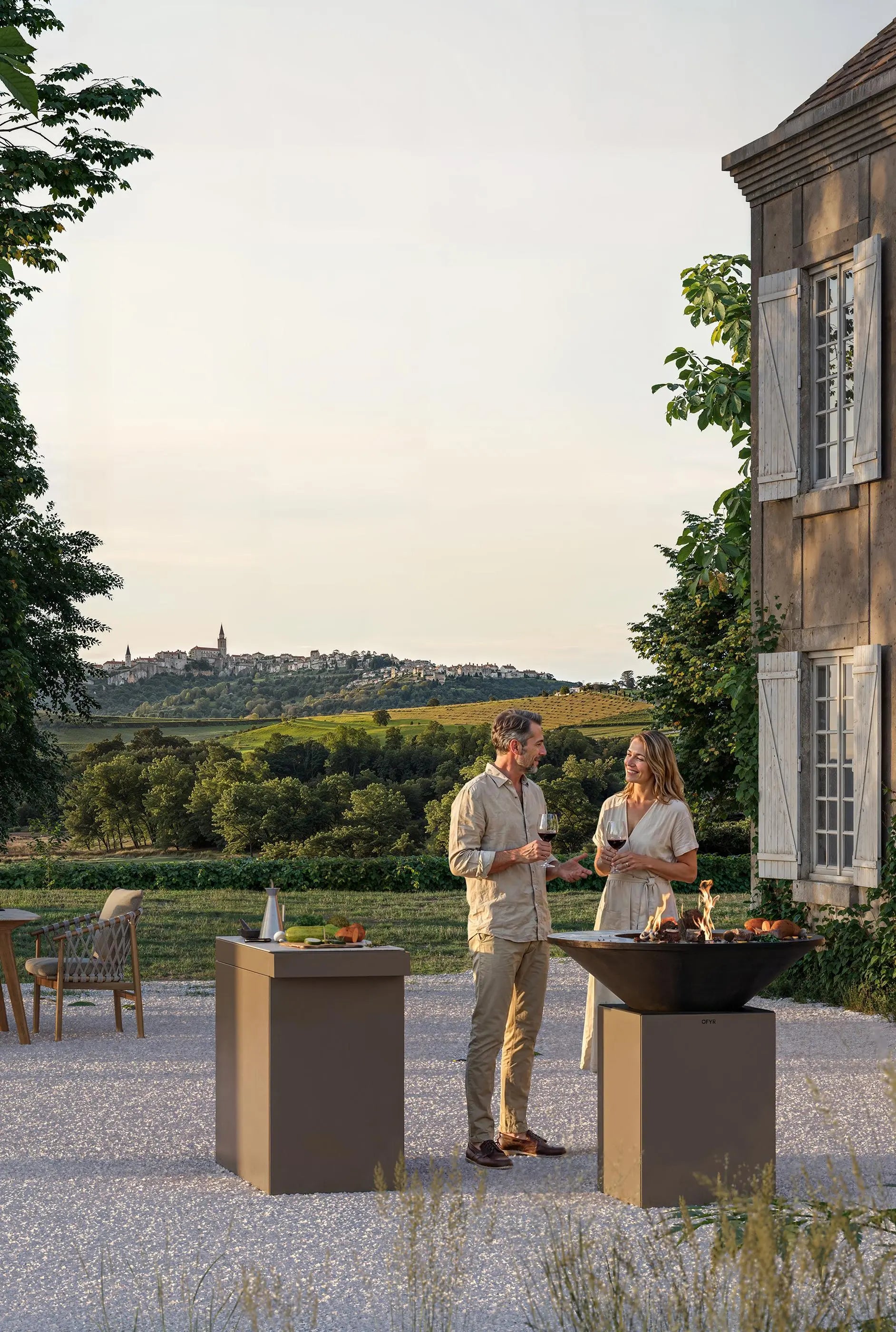 Two people standing outdoors near a grill with a scenic background