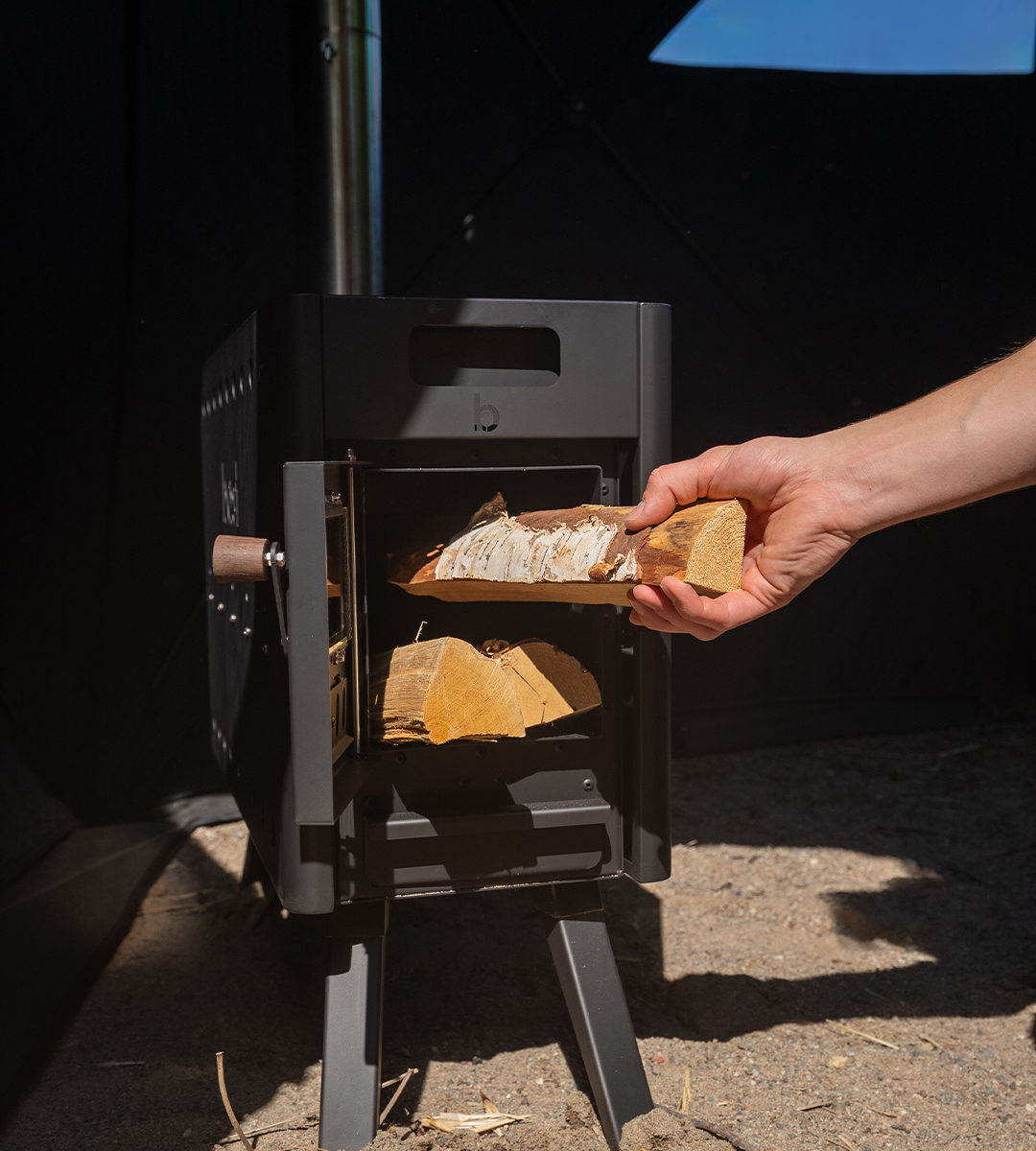Person loading wood into a portable stove for outdoor sauna tent. 